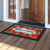 Bless This Home checkered floral doormat with red poppies on wooden porch outside open door.