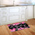 Black doormat with pink flowers and hummingbirds, "Home Sweet Home" in white on wooden floor.