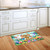 Spring Has Sprung Sign Doormat with colorful floral design and bunny on wooden floor by kitchen sink.