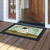 Country Saltbox Doormat with house design and welcome text on wooden porch outside open doorway.