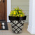 Large black planter with white floral design and yellow and pink flowers on a porch.
