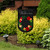 Black garden flag with colorful floral wreath and "Welcome" text on burlap material outdoors.