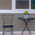 Small blue and gold planter with yellow flowers on a black metal table beside a chair.