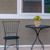 Pink and green modern planter on small black metal table beside matching chair outdoors.