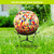 Rainbow speckled solar LED glass gazing ball on black stand outdoors on green grass lawn.