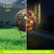 Multicolor solar LED glass gazing ball with mosaic tiles on a stand, lit up at night.