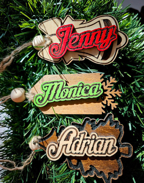 Custom Christmas 2025 wooden name tags in red, green, and natural text colors on natural, golden oak, and espresso bases.