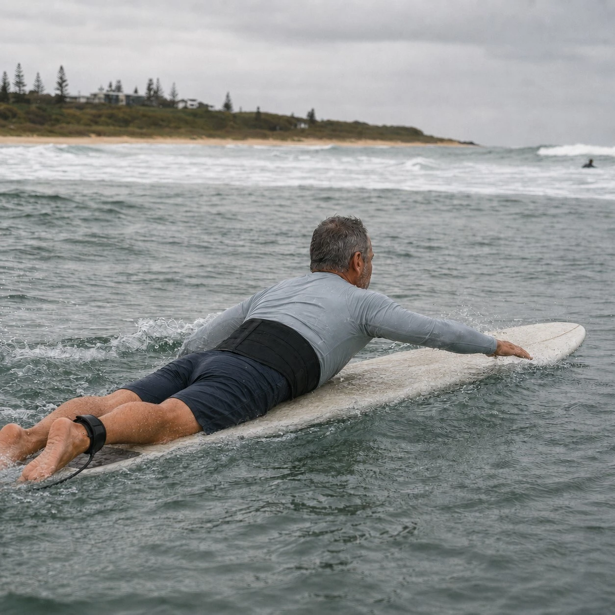 Surfer wearing the Elite Pro Back Support Brace while paddling on a surfboard