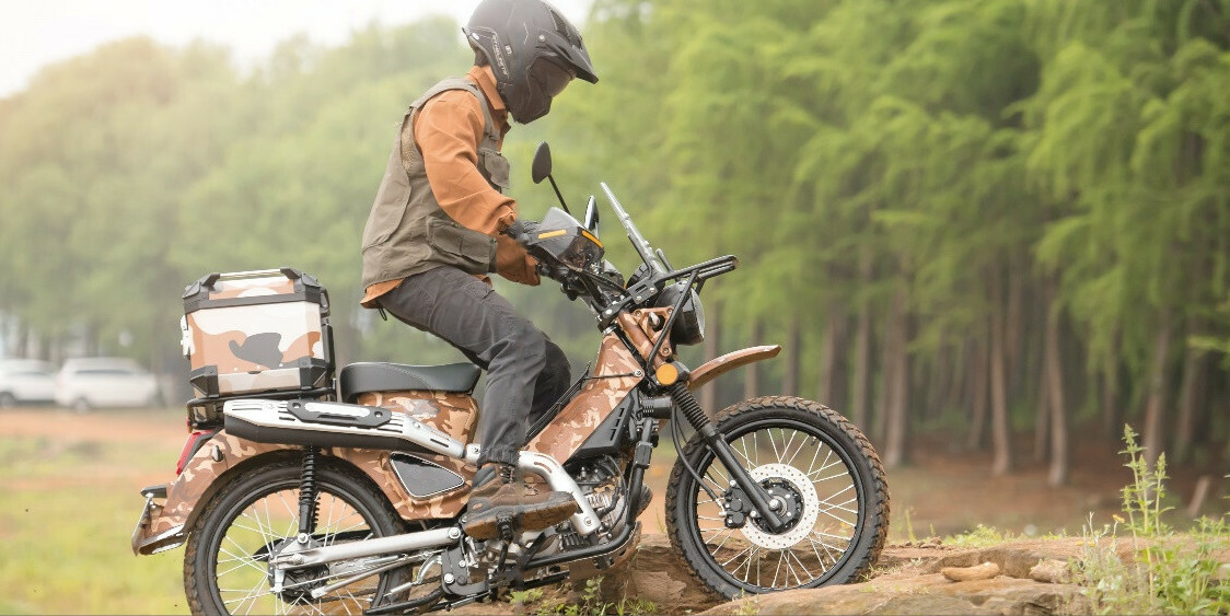 Riding the CSC Wolf 125 with camouflage paint up a dirt hill.