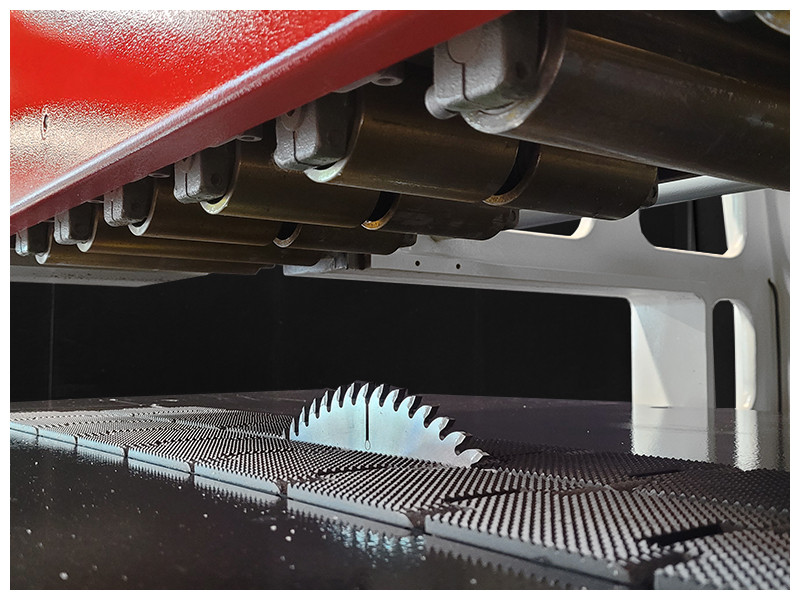 Hold down rolls and bottom mounted saw blade 
Equipped with 8 top steel hold down rollers which hold material firmly and precisely on the fast iron feed chain. This results in a precision glue joint cut. The bottom mounted saw bade can be raised and lowered according to the material thickness. The rotation of the sawblade in fact forces the material down on the chain surface which results in an even safer operation with greatly reduced tendency for material kickbacks.