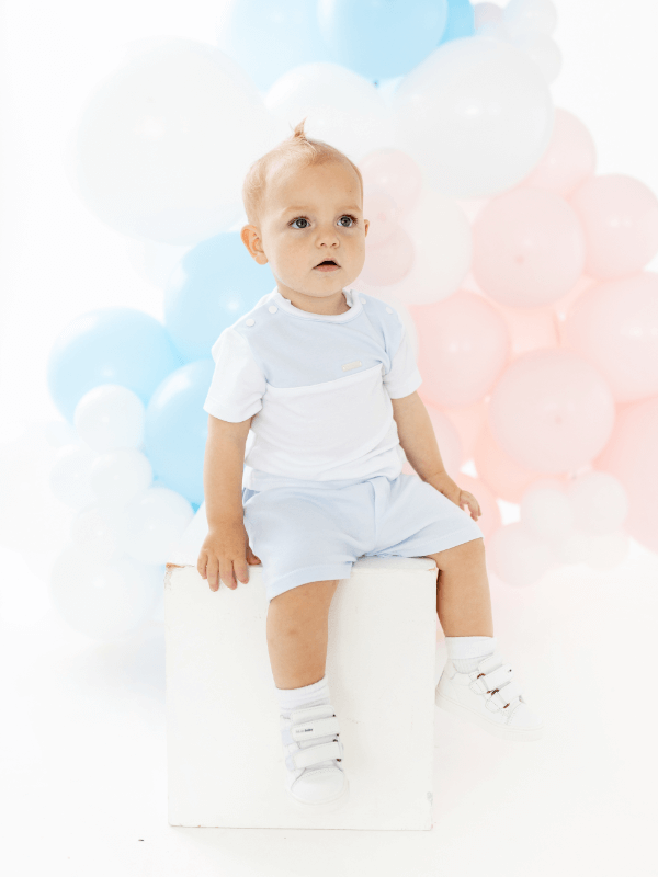 young child sitting on a box wearing white and baby blue tshirt and shorts
