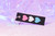 Thriving Despite It All keychain by Crushworthy - Trans pride colored hearts on one side, and text reading "thriving despite it all" on the other of a durable embroidered keychain