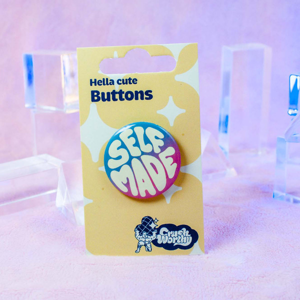 Self Made button by Crushworthy - "Self Made" in handwritten white text on a blue and pink gradient background. Trans pride!