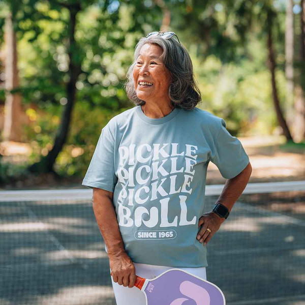 Lifestyle images of mature female model wearing Heritage Pickle-ball Pickle Pickle Tee at a park.