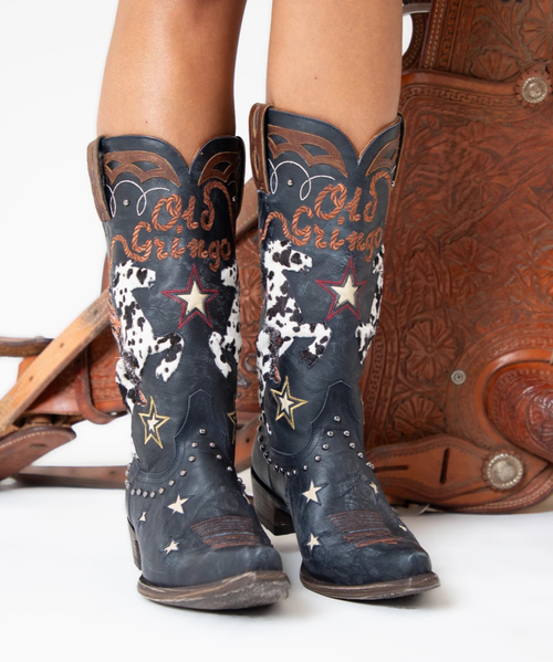 Old Gringo – Spirit Boots | Blue

Wild, free, and fierce—that’s the unmistakable Old Gringo spirit. Designed with a true giddy up attitude, these statement boots celebrate western soul and fearless style. A striking cowgirl atop a hair-on-hide horseback takes center stage, surrounded by rope and star emblems and finished with gleaming silver studs that add just the right amount of edge.

Set against a dark blue distressed leather background, the Spirit Boots blend bold artistry with classic western tradition. The timeless silhouette and neutral-yet-dramatic palette make them endlessly wearable, while their expressive details ensure they’ll always stand out. These are boots you’ll reach for year after year—true icons in any country-inspired collection.
