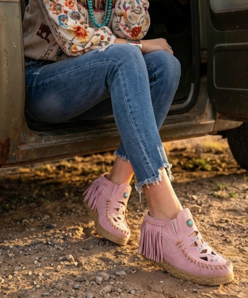 This image captures a striking boho-meets-urban western look set against a bold, blue graffiti-style wall ?✨

The model is posed with one leg lifted onto a curb, creating a confident, fashion-forward stance. She’s wearing a flowing black maxi dress with a delicate floral print and sheer layers that add movement and depth. The dress features a plunging neckline, long sleeves, and ruffled detailing, giving it a romantic, free-spirited feel.

Around her waist is a statement belt with oversized conchos, adding a strong western influence, while layered necklaces and a cuff bracelet enhance the bohemian styling. A small red crossbody bag adds a pop of color and contrast.

Her footwear grounds the look with edge—tall black-and-cream cowboy boots with a slightly worn, vintage finish and a pointed toe, blending classic western craftsmanship with a modern attitude.

The mix of soft, flowing fabric and structured accessories, set against the gritty street-art backdrop, creates a look that feels both effortlessly feminine and boldly rebellious