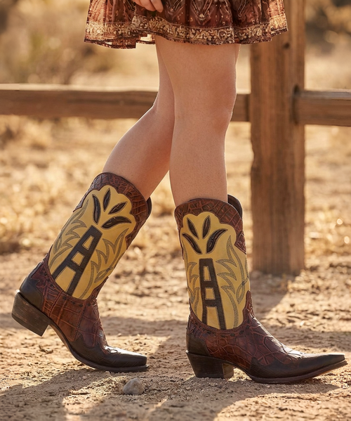 Certainly! Here's the revised version with a clean, premium details section and no emojis.

---

## Double D Ranch Dance in the Derricks Boot – Tan

**Dare to Dance in the Derricks.**

Inspired by the grit, glamour, and heritage of the American oil fields, the **Dance in the Derricks Boot** from the Double D Ranch **2026 Roughneck Rodeo Collection** celebrates the bold spirit of those willing to take a chance. Luxurious two-tone waxy leather is paired with a rich crocodile-inspired vamp, while vintage oil derrick artwork stitched into the shaft pays tribute to the hardworking pioneers who struck it rich.

Intricate decorative stitching, layered leather overlays, contrast detailing, and classic Western lacing create depth and texture, making this boot a true work of wearable art. With its sleek **12-inch shaft**, elegant **4Long toe**, and signature **9964 heel**, the Dance in the Derricks Boot effortlessly blends timeless Western tradition with elevated modern style.

Whether you're headed to the dancehall, a concert, or simply stepping out in style, these boots are made for women who embrace adventure and leave a lasting impression.

### Details

* Color: Tan
* Premium waxy leather construction
* Crocodile-inspired leather vamp
* Decorative oil derrick embroidery and contrast stitching
* Layered leather overlays and underlays
* Decorative leather lacing
* Approximately 12-inch shaft height
* Classic 4Long toe
* Signature 9964 stacked heel
* Designed alongside the Double D Ranch **2026 Roughneck Rodeo Collection**

**Please Note:** Every pair is handcrafted using premium natural leather. Variations in color, grain, texture, and distressing are part of the authentic character of the leather, making each pair uniquely beautiful.

