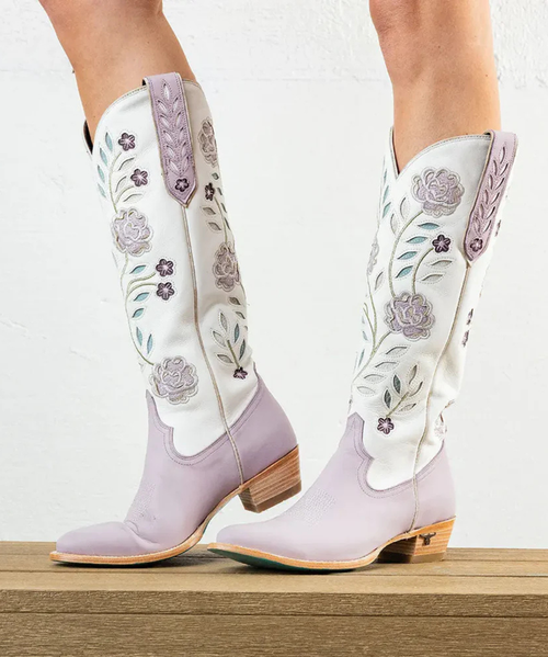 Soft, romantic, and a little flirtatious — the Lovely Lavender Kenzie is the collection's most feminine expression. A delicate two-tone palette of pale lavender and cream sets the stage for inlaid floral motifs and meticulous embroidery that bloom across the shaft like a pressed-flower keepsake.

Contrast piping draws the eye to every curve. A classic toebug grounds the vamp in Western heritage. The pull tabs — inlaid and embroidered with the same care as the rest of her — are a small flourish you'll notice every time you reach for her. Almond toe. Classic Western heel. A sexier 16" shaft. She's a love letter to embellished Western boots, rewritten in lavender.

FIT NOTE: Designed with a slimmer, more tailored shaft for a sleek, leg-lengthening look. This style is a pull-on construction with no zipper.

Specs:

Toe Shape: Almond
Shaft Height: 16"
Shaft Circumference: 15.25"
Ankle Circumference: 11.75"
Heel Height: 1.6"