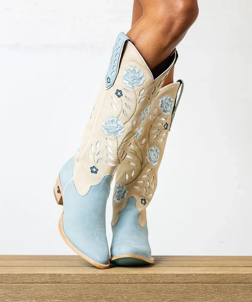 Blueberry Buttermilk Kenzie pairs a soft buttermilk leather body with cool blueberry tones for a two-tone palette that feels fresh, feminine, and pulled straight from a 1970s daydream.

Inlaid floral motifs bloom up the shaft, every petal traced in meticulous embroidery. Contrast piping carves a clean line through the design, and a classic toebug anchors the vamp in true Western tradition. Even her pull tabs are detailed — inlaid, embroidered, and just as considered as the rest of her. With an almond toe, a classic Western heel, and a sexier 16" shaft, she's the kind of boot that earns a permanent spot in your closet.

FIT NOTE: Designed with a slimmer, more tailored shaft for a sleek, leg-lengthening look. This style is a pull-on construction with no zipper.

Specs:

Toe Shape: Almond
Shaft Height: 16"
Shaft Circumference: 15.25"
Ankle Circumference: 11.75"
Heel Height: 1.6"