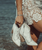 describe the image

A dreamy, beachside lifestyle photo capturing a woman walking barefoot at the edge of the ocean, waves gently rolling over the sand ?✨

4

Outfit & Details

She’s wearing a delicate white lace mini dress with intricate floral patterns, giving the look a romantic, coastal-boho feel.

In her hand, she carries a pair of white leather western ankle boots.

The boots feature a pointed toe, stacked wooden heel, studded detailing in a classic western stitch pattern, and pull tabs at the top.

A small ankle tattoo and simple bracelets add to the relaxed, effortless vibe.

Setting & Mood

Shot at the shoreline with soft waves foaming around her feet.

Warm natural light creates a golden, sun-kissed glow.

The contrast of crisp white boots against the ocean backdrop makes the footwear pop beautifully.

Overall vibe:
Romantic coastal cowgirl ?? Perfect for showcasing statement western booties in a soft, dreamy lifestyle setting—very Boot Junky aesthetic, Paulette!