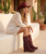 This image captures a soft, sunlit western-boho moment with a dreamy, desert-inspired aesthetic ?✨

A woman sits casually on a smooth, white stucco bench, surrounded by warm, neutral tones and minimal architectural lines that feel Mediterranean or Southwestern in style. The natural light creates a golden glow, enhancing the relaxed, serene atmosphere.

She wears a lightweight cream knit sweater dress, slightly oversized with a breezy, effortless drape. The texture adds a cozy yet airy feel, perfect for a laid-back, warm-weather look.

Her accessories and styling bring the outfit to life:

A turquoise cowboy hat adds a bold pop of color and a classic western touch
Matching turquoise fringe boots steal the spotlight, featuring moccasin-style stitching, lace-up details, and long fringe that adds movement and personality
The boots are complemented by subtle metallic accents and handcrafted details

Her relaxed pose—resting her head on her hand—gives off an easy, contemplative vibe, while her loose waves enhance the natural, carefree look.

Overall, the image blends bohemian softness with western statement pieces, creating a look that feels both elevated and effortlessly cool