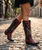 These boots are a bold, statement-making pair of western showstoppers that fuse classic cowboy craftsmanship with edgy, artistic detail ?✨

Crafted in a rich two-tone leather combination, the base features deep chocolate brown paired with a striking turquoise crackled finish that gives a vintage, worn-in character.

Key Design Features:
Intricate inlay and embroidery work in turquoise, creating flowing, western-inspired patterns along the shaft and vamp
Mixed metal embellishments, including studs, domed hardware, and decorative accents that add texture and dimension
Prominent cross appliqués and concho-style details, giving the boots a bold, southwestern, almost heirloom feel
A studded center seam running vertically up the shaft for added edge and structure
Subtle distressing throughout for that perfectly broken-in, authentic look
Silhouette & Structure:
Classic snip/pointed toe for a sharp, feminine western profile
Mid-height stacked heel that’s both flattering and wearable
Tall shaft designed to stand out whether paired with denim or dresses
Overall Vibe:

These boots blend rock-and-roll western attitude with artisan craftsmanship—perfect for someone who wants a standout, collectible piece. They feel equal parts vintage, rebellious, and luxurious, making them the kind of boots that instantly elevate any outfit
