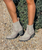 The Clint Boot by El Vaquero is a striking over-the-knee silhouette that blends refined craftsmanship with effortless summer elegance. Distinguished by a sleek ankle strap and beautifully detailed leather accents along the shaft, this boot delivers unmistakable style with a soft, artisanal feel.

Crafted in Italy from a unique combination of luxurious calfskin suede and fine natural linen, Clint offers a fresh, lightweight construction that’s perfect for warm-weather styling. The subtle 7 cm internal wedge provides comfortable lift without compromising ease, while the vintage treatment adds character and depth to every pair.

Finished with handcrafted stitching, nickel-free metal details, and a durable rubber sole, the Clint boot is designed for confident, all-day wear. Elegant yet relaxed, it pairs effortlessly with flowy dresses, tailored shorts, or layered summer looks.

Details:

Over-the-knee boot

Internal wedge: 7 cm

Vintage treatment

100% calfskin suede and natural linen

Handcrafted stitching

Nickel-free metal details

Rubber sole

Made in Italy