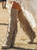 A beautiful boho-western styled model walks confidently across a sunlit outdoor festival setting. She wears a romantic ivory lace dress with long bell sleeves and an asymmetrical hemline that flows softly in the breeze. The deep V-neckline and delicate lace texture add a feminine, vintage feel, while a wide tooled leather belt with an ornate buckle cinches her waist for a western edge.

Her long, voluminous curly hair frames her face beneath a hat, and she completes the look with classic brown embroidered cowgirl boots that give the outfit a rugged, country-chic vibe. In the background, a stage setup and blurred crowd hint at a music festival atmosphere, creating a carefree, stylish, bohemian mood perfect for a warm summer concert day.