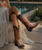 This image is a beautiful blend of **Western romance, vintage femininity, and bohemian luxury**.

Seated poolside in a woven lounge chair, the model exudes effortless confidence in a dreamy ensemble that feels inspired by both **Texas Hill Country and coastal bohemia**. She wears a flowing ivory dress with layers of delicate ruffles and sheer fabric that create movement and softness. The bodice features warm peach and blush tones with subtle embroidery and feminine ruffle trim, adding a touch of vintage lingerie-inspired charm.

A woven straw hat with geometric detailing gives the look a relaxed, sun-drenched feel, while silver jewelry adds an artisan touch.

The star of the outfit is the pair of rich **cognac and black Western boots**. Featuring:

* Distressed cognac leather foot
* Contrasting black shaft
* Classic Western embroidery
* Snip toe silhouette
* Fashion heel
* Vintage-inspired finish

The boots provide the perfect balance to the airy dress, bringing a sense of strength and Western heritage to an otherwise soft and romantic look.

### Style Vibe

? Western Romance

? Prairie Meets Palm Springs

✨ Vintage Cowgirl Chic

? Bohemian Feminine

?️ Desert Dreamer

### Boutique Selling Description

**Where cowgirl spirit meets effortless elegance.**

Layers of airy ivory ruffles, soft sunset hues, and handcrafted details create a look that's both romantic and adventurous. Paired with rich cognac Western boots and a woven sun hat, this outfit captures the essence of modern bohemian style—feminine, free-spirited, and undeniably chic.

Perfect for:

* Wine country weekends
* Summer concerts
* Resort getaways
* Round Top treasure hunts
* Sunset dinners on the patio

### Why This Works for Boot Junky

This image perfectly illustrates a styling direction that resonates with customers who love:

* Old Gringo
* Double D Ranch
* El Vaquero
* Johnny Was
* Spell
* Chasing Unicorns

It combines the softness of bohemian fashion with the authenticity of artisan Western boots, creating a look that feels luxurious, collectible, and highly wearable. It's the kind of outfit that sells not just a pair of boots—but an entire lifestyle. ??✨???

