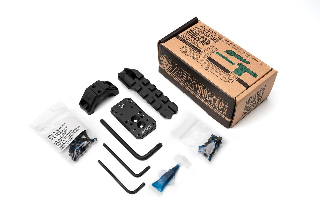 Strike Industries SI-STRIKE-ASM-OM ASM Ring Cap Multi-Optic Mount System, disassembled with various black metal mounting components, hex keys, screws, and a small tube of lubricant, alongside the product's packaging box.