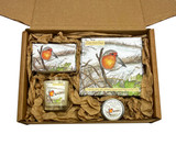 Overhead view of the Cold Still Days Robin Gift Box, showing a candle, a tin of lip balm, a soap bar, and a box of tealights, all with a charming robin illustration, nestled inside a brown cardboard box on scrunched up natural tissue paper.