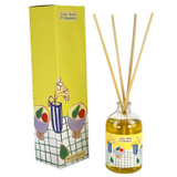 A Heaven Scent 100ml clear apothecary glass reed diffuser with four natural reeds, standing next to its tall bright yellow gift box. The box and bottle label feature a contemporary illustration by Sarah Pettitt including bowls of pears, a blue striped vase with white flowers and a green chequered pattern.