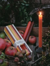 A beautifully illustrated, autumn-striped gift box for Heaven Scent's The Autumn Edit mixed dinner candles, displayed alongside six straight, hand-poured artisan dinner candles in complementary shades of Pumpkin Orange, Dark Brown and Burnt Orange.
