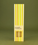 A beautifully illustrated, cream and yellow striped gift box for Heaven Scent's The Natural Edit dinner candles, displayed alongside six straight, hand-poured artisan dinner candles in a classic, solid Natural shade.