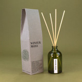 A 100ml luxury Winter Moss Green Botanical reed diffuser by Heaven Scent, housed in an elegant green apothecary glass bottle with natural rattan reeds, made in the UK.