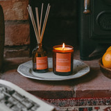 Festive Christmas Clementines 20cl amber glass scented Christmas candle from the Modern Heritage collection, shown beside its bright orange gift box.
