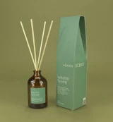 Winter Thyme 100ml amber apothecary glass Christmas reed diffuser from the Modern Heritage collection, shown with natural rattan reeds and its herb green box gift box.
