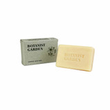 A rectangular, light-coloured natural soap bar stamped with 'Botanist Garden', positioned next to its grey recycled card box.