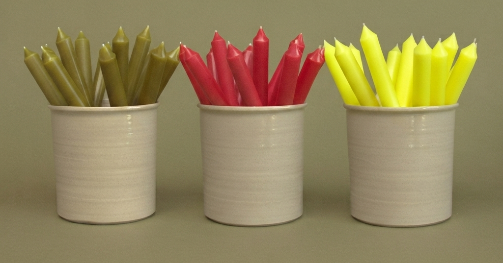 Clusters of green, red and yellow vegan dinner candles displayed upright in three neutral ceramic pots.