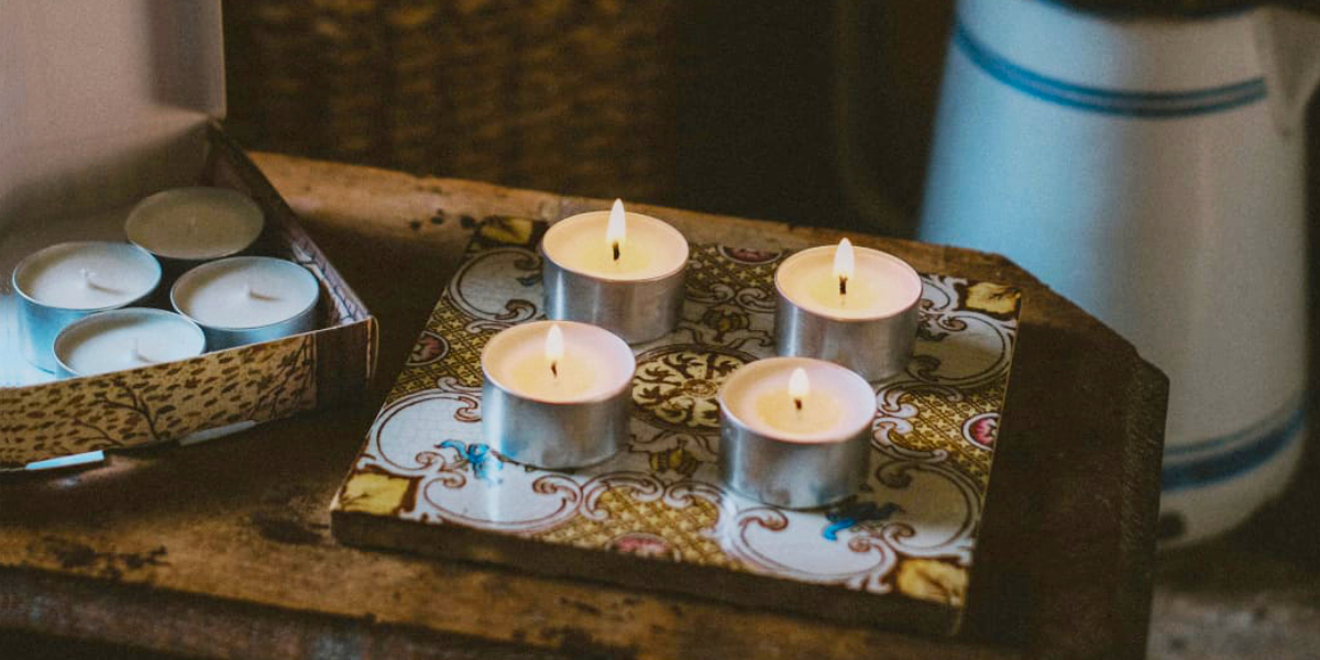 Lit natural soy wax tealights displayed on an ornate patterned tile alongside an open box of matching festive tealights.