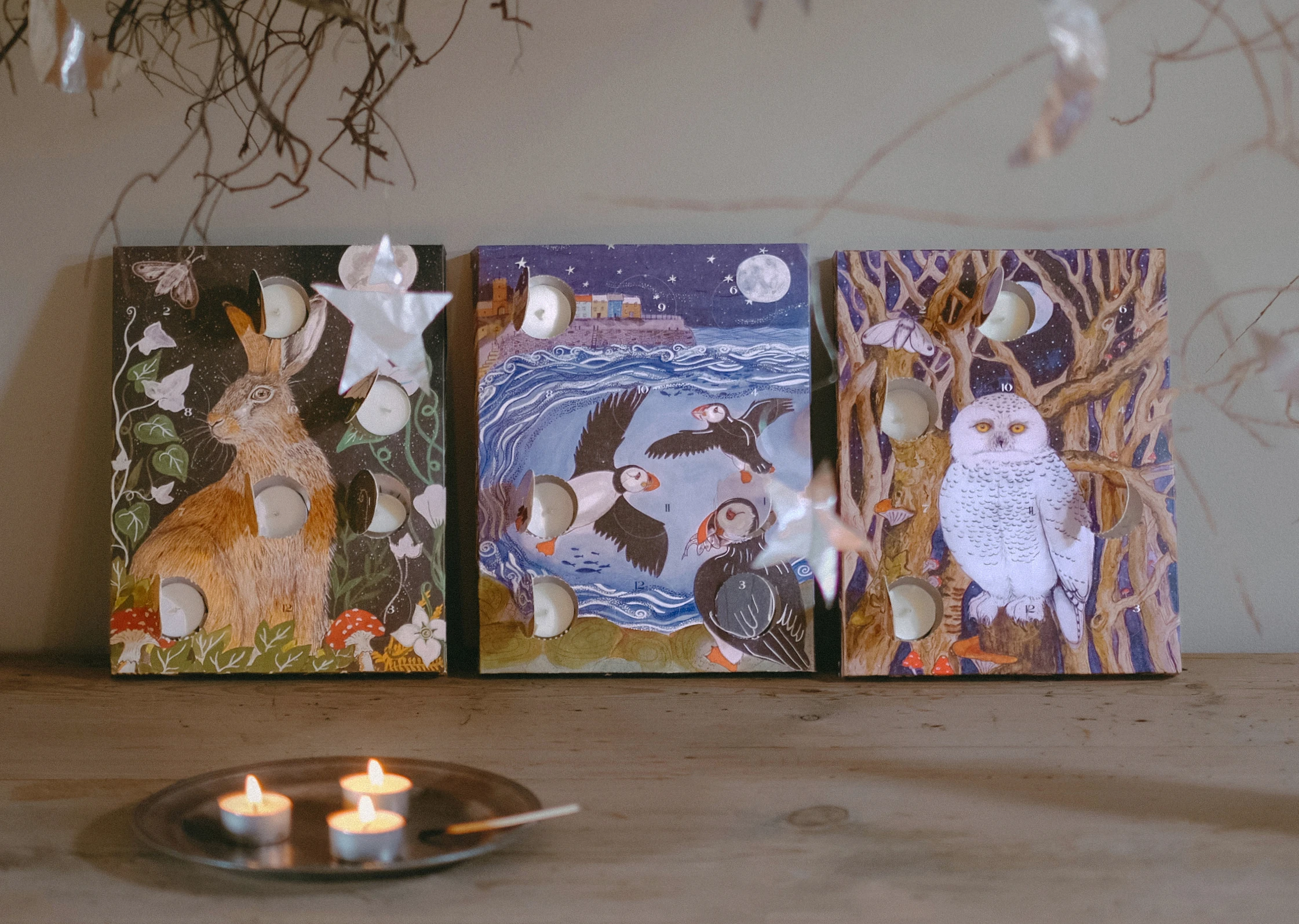 Heaven Scent 12-day Scented Tealight Advent Calendars featuring a Hare, Snowy Owl and puffins flying over a harbour scene, with 3 lit tealights.