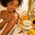 Dame gently applying Sunshine Body Butter to her arm for a soft, glowing finish.