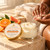 Black woman warming Citrus + Agave Body Butter between her hands beside the open jar and approved orange-and-gold lid.