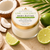 Lime + Coconut Body Butter in a clear glass jar with a gold lid and approved cream-and-lime-green label, surrounded by coconut and fresh lime.