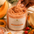 Close-up of Dame Body Cantaloupe Polishing Body Scrub as a Black hand scoops the thick peach-toned exfoliating scrub, surrounded by cantaloupe, apricot, rosehip, sea buckthorn, and pink Himalayan salt.