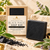 Dame Body Black Magic Soap Bar in kraft window box with unboxed activated charcoal botanical cleansing bar