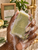 Serenity Green Tea Soap Bar held in a deep brown manicured hand with creamy lather during a fresh botanical shower ritual