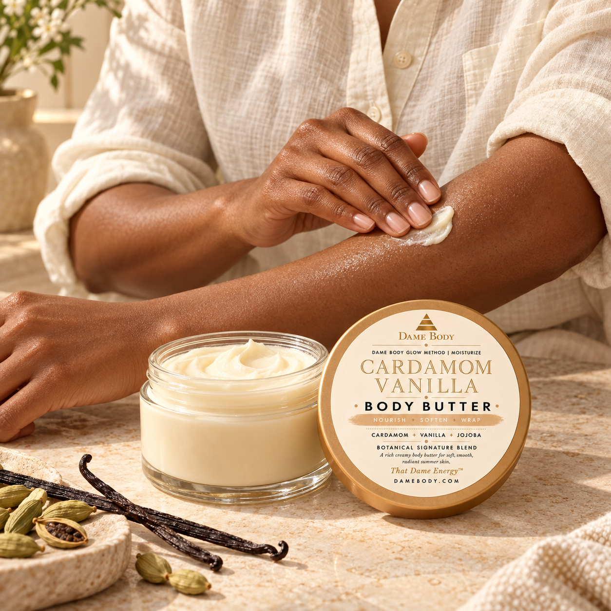 A Dame gently applying Cardamom + Vanilla Body Butter to her forearm beside its tan-and-gold labeled lid