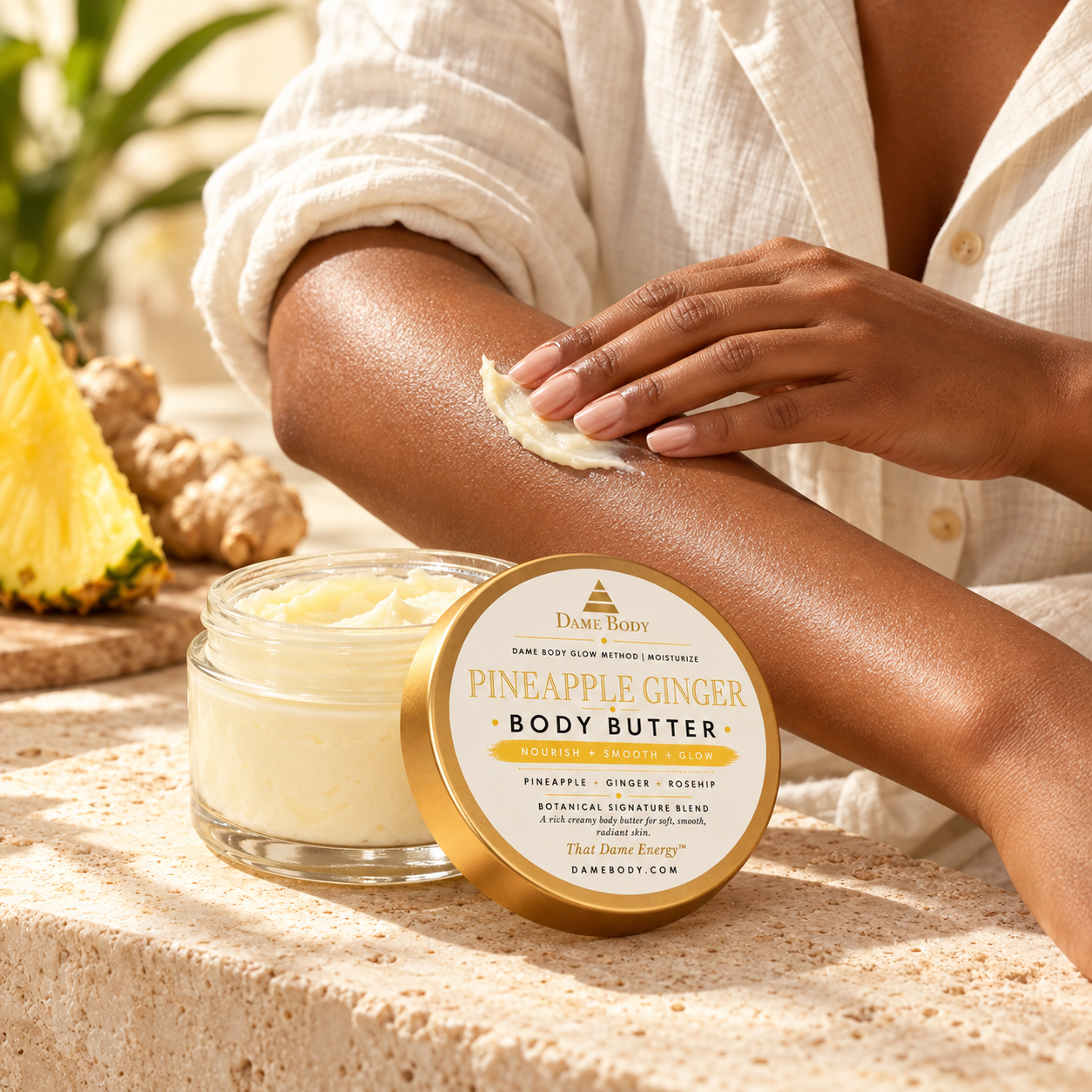 Black woman gently smoothing Pineapple Ginger Body Butter onto her forearm beside the current-label jar.