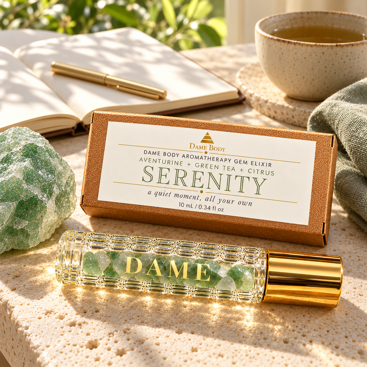 Serenity roller and labeled kraft box beside a journal, tea and raw Aventurine in soft morning light.